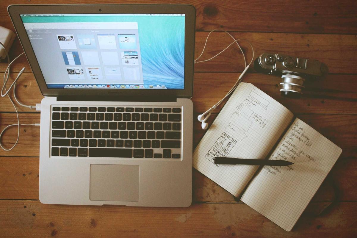 A notebook, laptop and cup of coffee on a wooden desk